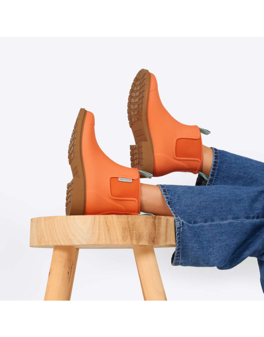 Bright orange Merry People Bobbi gumboots displayed on a stool, showcasing their cheerful Sherbet Orange color and waterproof design.