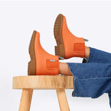 Bright orange Merry People Bobbi gumboots displayed on a stool, showcasing their cheerful Sherbet Orange color and waterproof design.