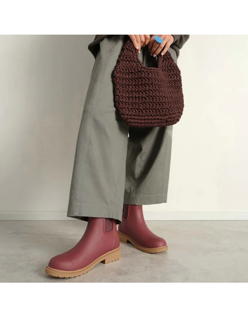 Merry People Bobbi Gumboots in brick red worn by a model, showcasing waterproof rubber footwear designed for outdoor wear.