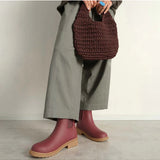Merry People Bobbi Gumboots in brick red worn by a model, showcasing waterproof rubber footwear designed for outdoor wear.