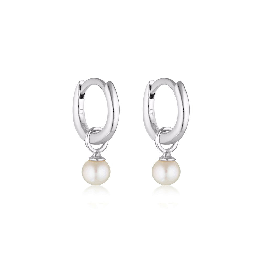 Linda Tahija Pearl Charm Mini Huggie Earrings featuring small gold hoops with delicate pearl charms on a white background.
