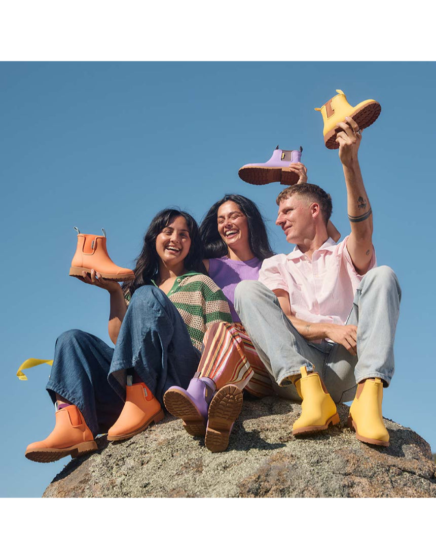 Merry People Bobbi gumboots in vibrant sherbet orange, shown in outdoor lifestyle setting with a person wearing them.