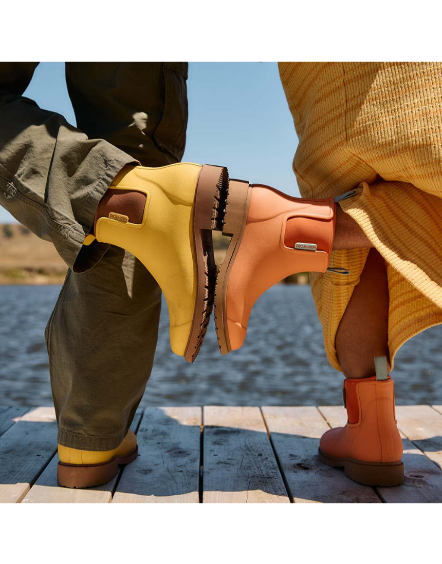 Merry People Bobbi gumboots in vibrant sherbet orange, stylish waterproof rain boots for women, shown outdoors in a lifestyle shot.