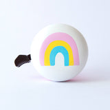 Beep Happy Rainbow Bike & Scooter Bell in white and pink with colorful rainbow design, mounted on a bicycle handlebar.