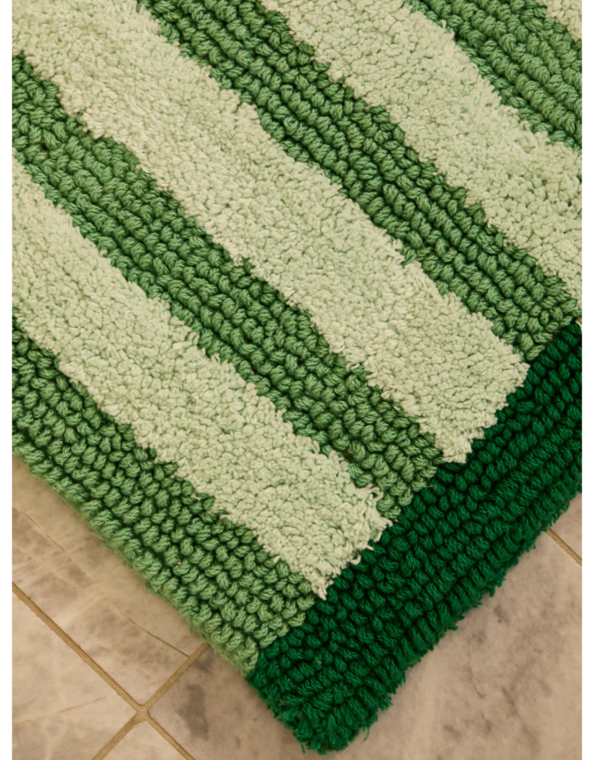 Reversible green stripe bath mat by Bonnie and Neil, shown in a bathroom setting with textured fabric and striped pattern.