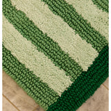 Reversible green stripe bath mat by Bonnie and Neil, shown in a bathroom setting with textured fabric and striped pattern.
