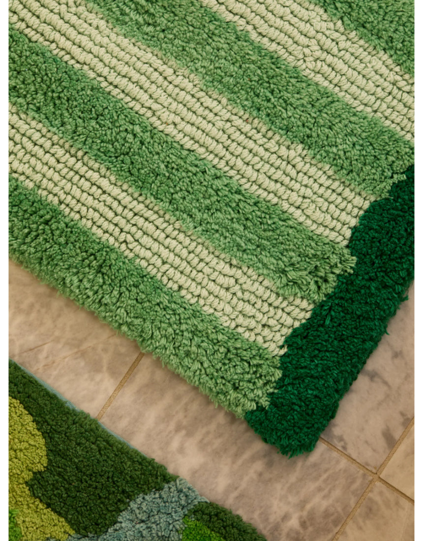Reversible green bath mat with striped pattern by Bonnie and Neil, shown in a bathroom setting.