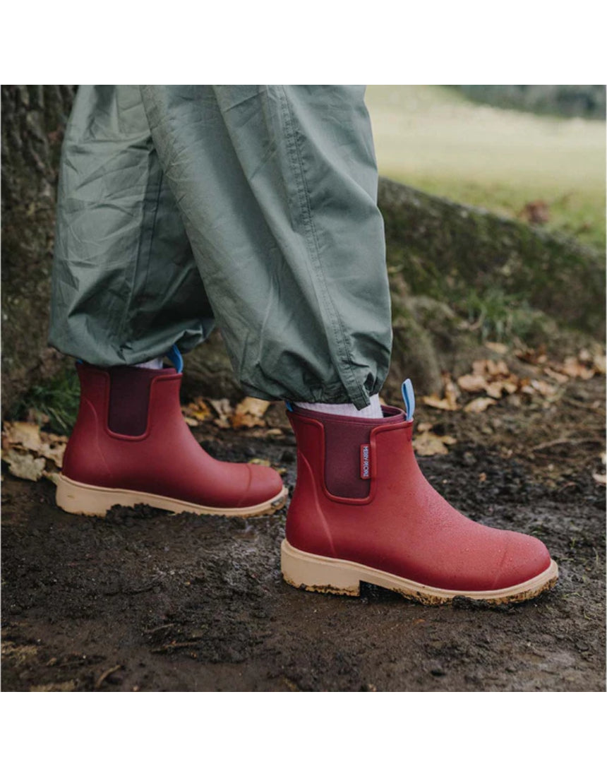 Merry People Bobbi gumboots in brick red worn outdoors, showcasing waterproof rubber footwear with stylish design.