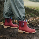 Merry People Bobbi gumboots in brick red worn outdoors, showcasing waterproof rubber footwear with stylish design.