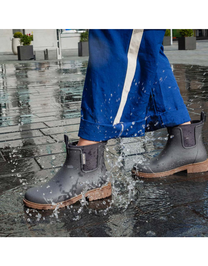 Merry People Bobbi gumboots in charcoal color, stylish waterproof footwear, shown outdoors with a person wearing casual clothing.