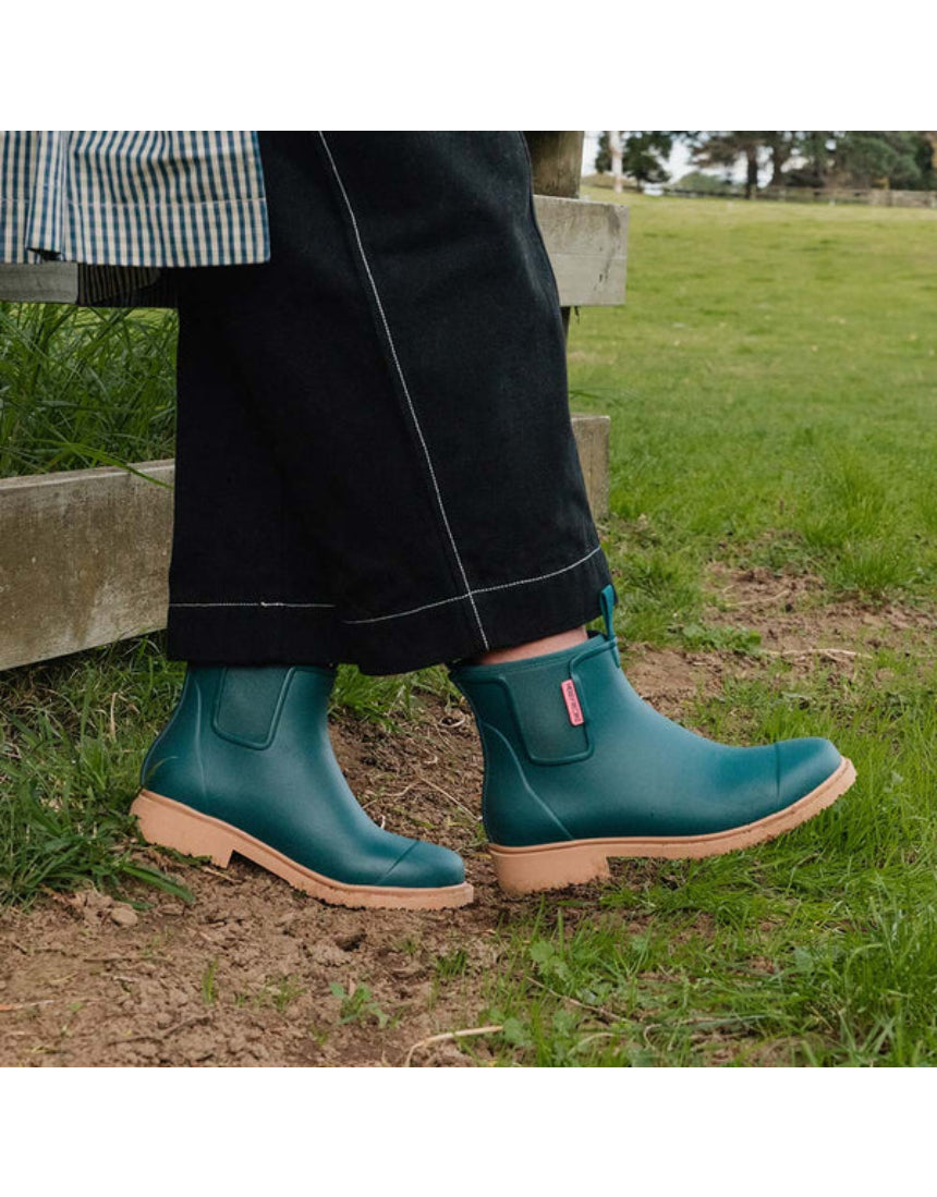 Merry People Bobbi Gumboots in teal, stylish waterproof rain boots for women, shown outdoors with greenery background