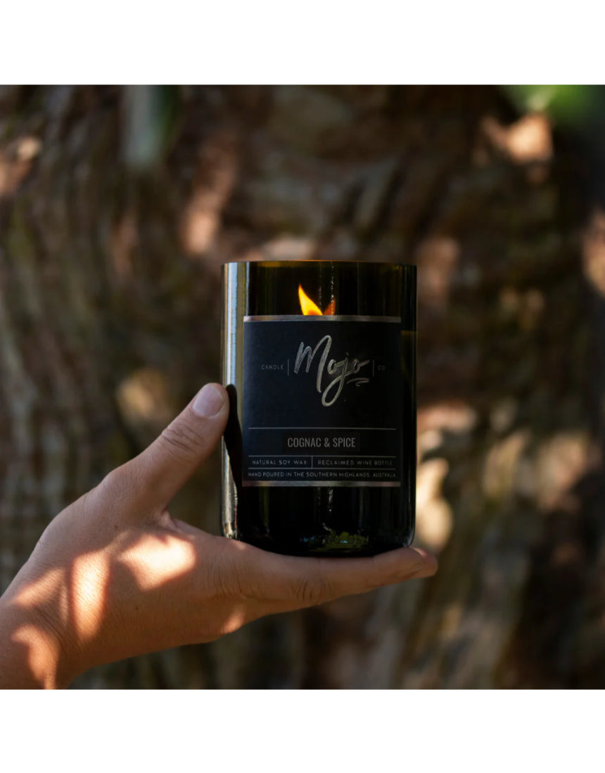 Mojo Candle Co. Cognac & Spice Black Label candle in a dark glass jar with a lit wick, emitting a warm, spicy glow.