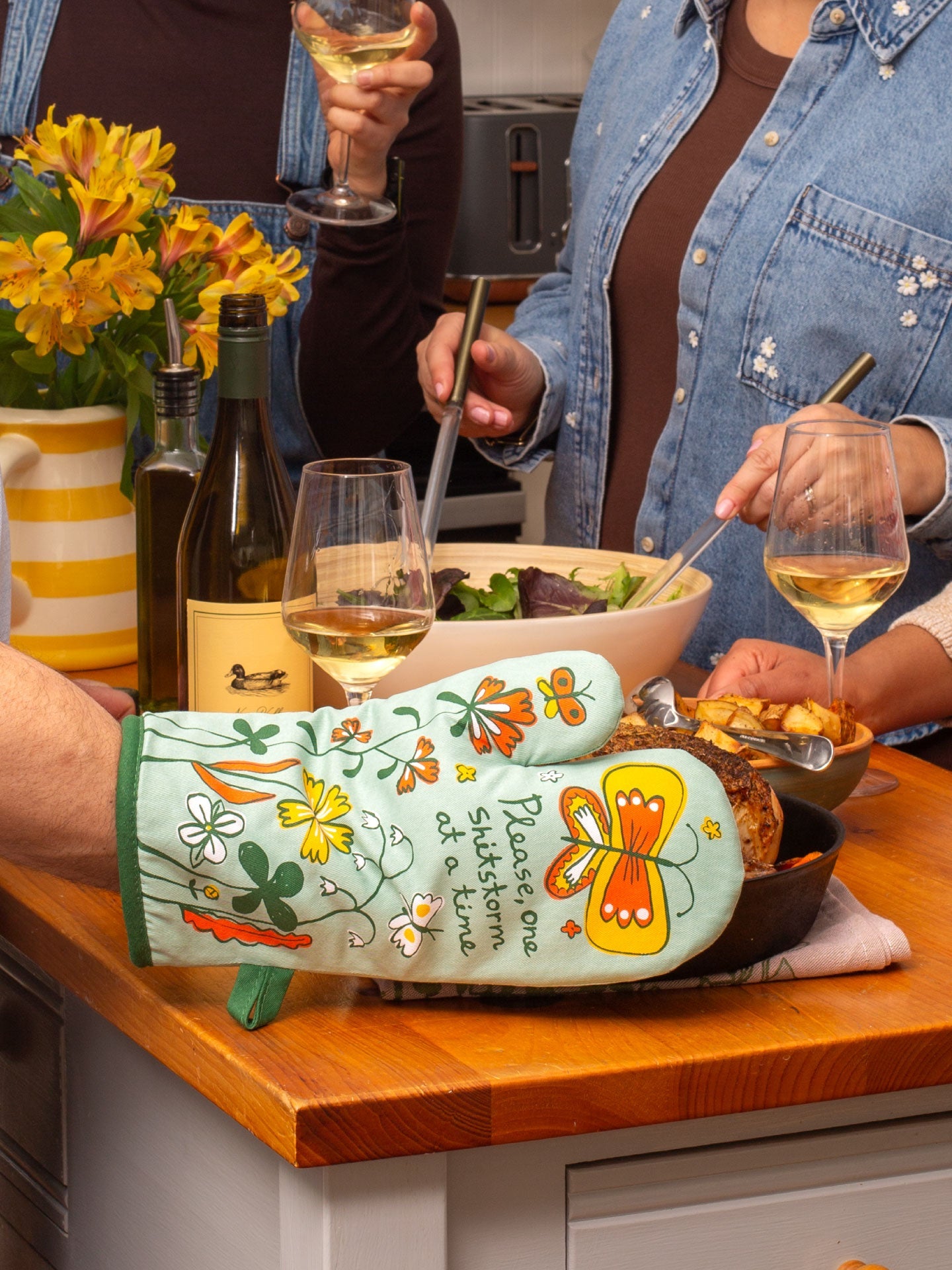 Blue Q oven mitt with colorful "Shitstorm" design, heat-resistant fabric for kitchen use.
