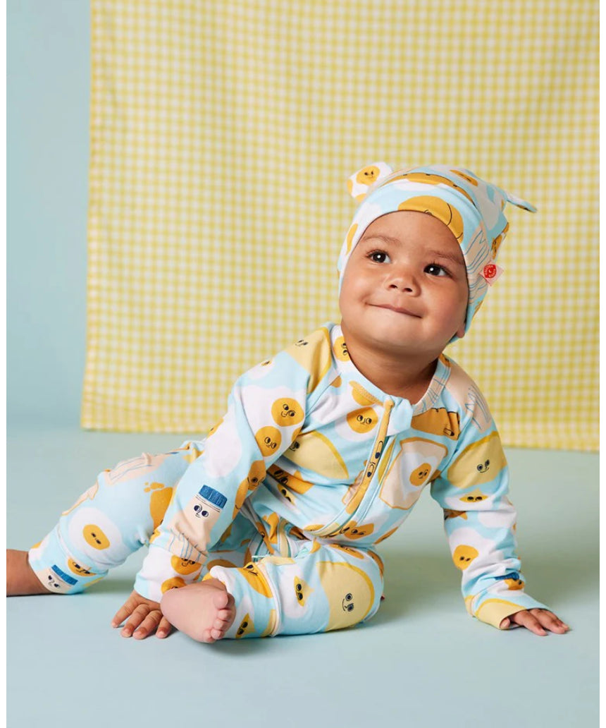 Baby wearing a Halcyon Nights Brunch Buddies long sleeve zip suit with a matching hat, featuring colorful brunch-themed patterns.