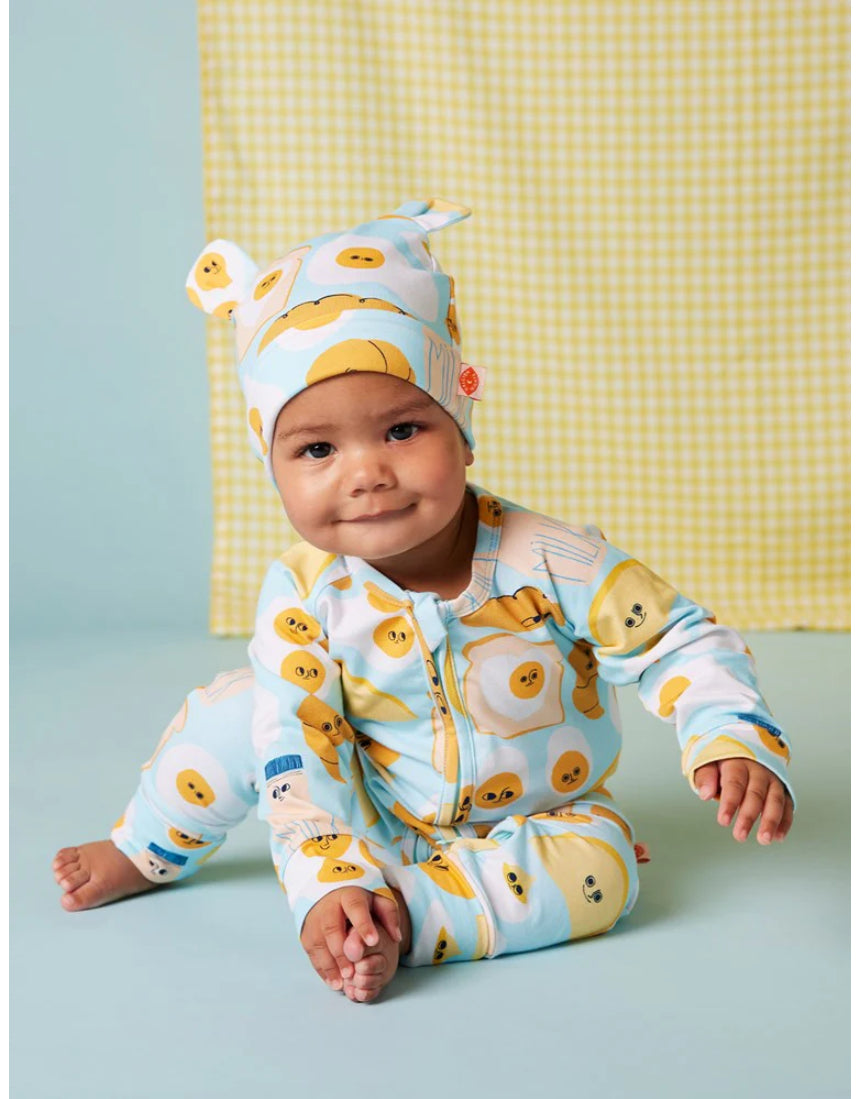 Baby wearing Halcyon Nights Brunch Buddies long sleeve zip suit with matching hat, featuring playful brunch-themed print.