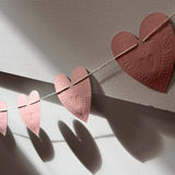 Reversible faux-tin heart bunting in light dusty pink by THE LITTLE PRESS, hanging with visible heart-shaped flags.