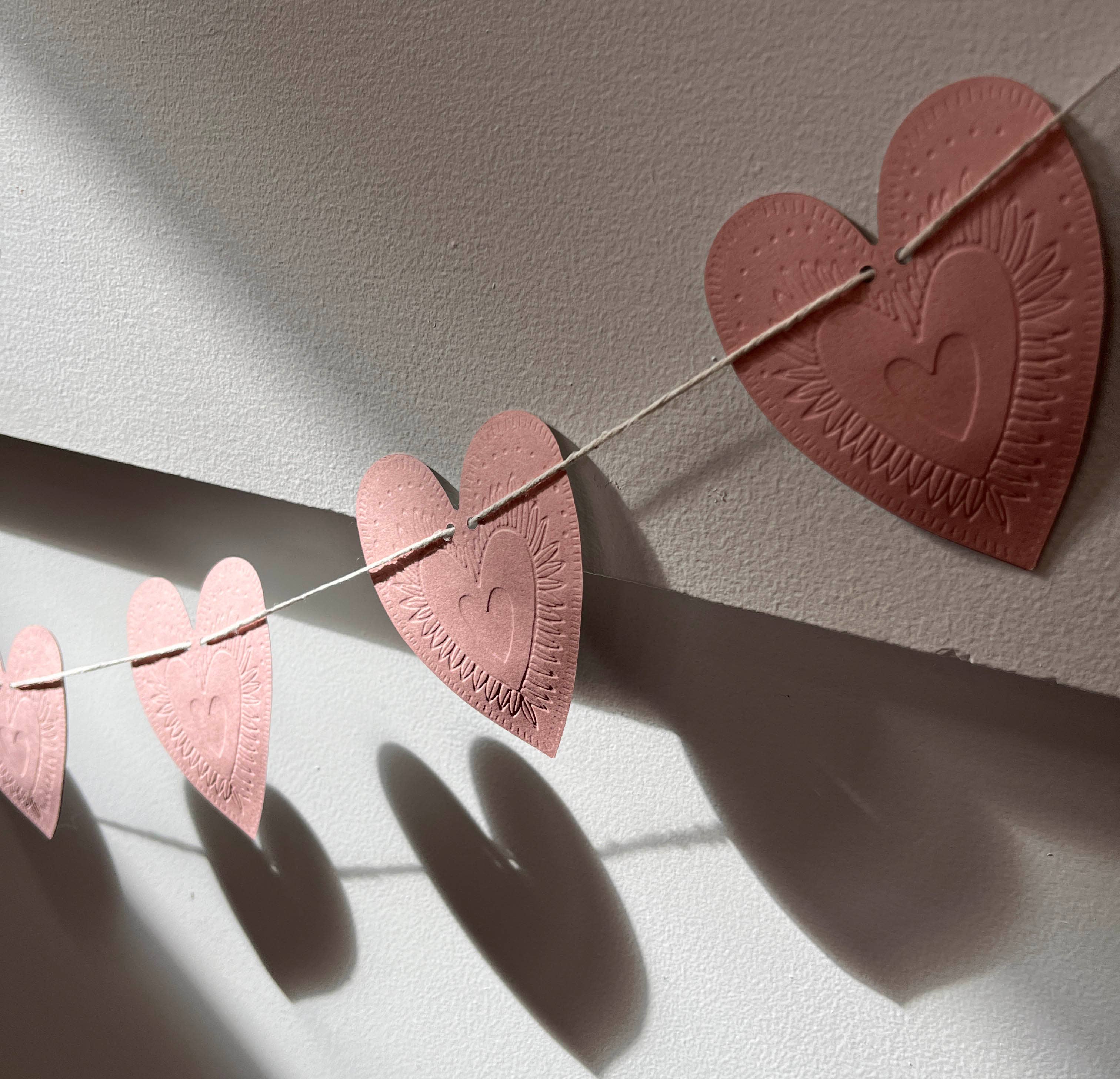 Reversible faux-tin heart bunting in light dusty pink by THE LITTLE PRESS, hanging with visible heart-shaped flags.