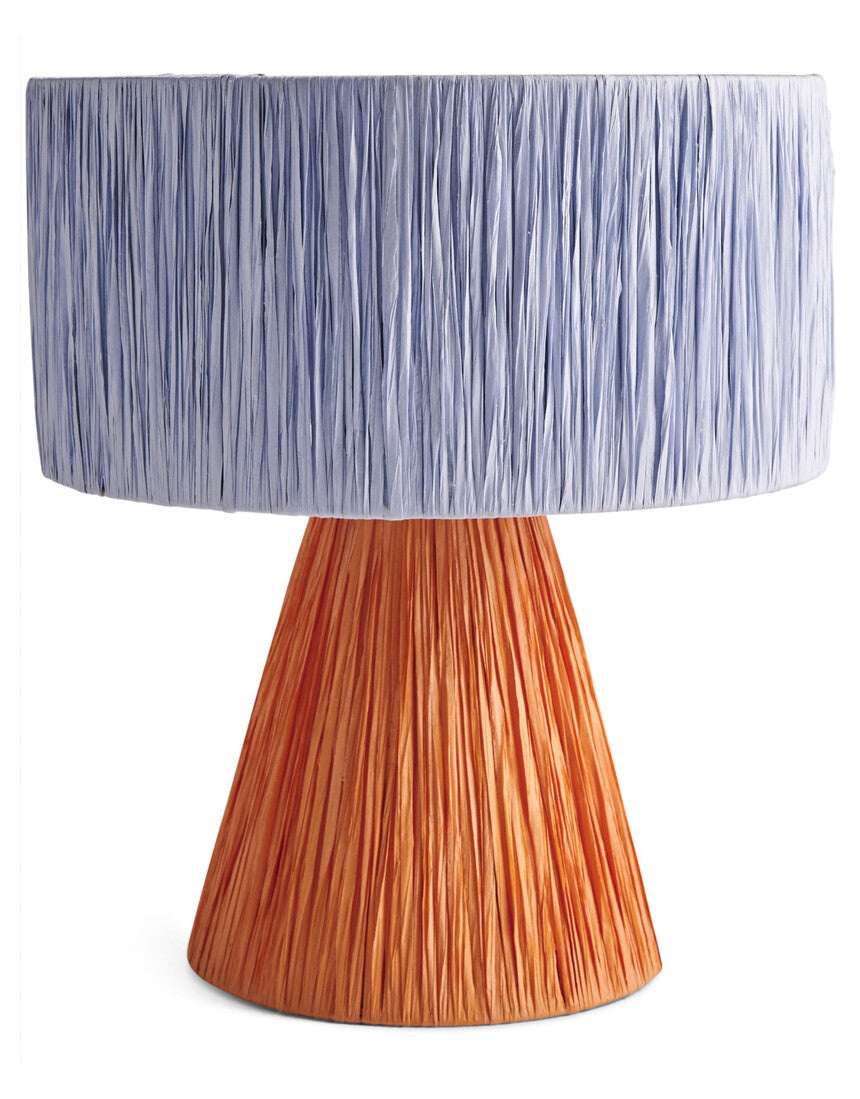 Kip & Co Tangier Raffia Table Lamp with woven rattan base and beige fabric shade on a wooden side table.