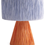 Kip & Co Tangier Raffia Table Lamp with woven rattan base and beige fabric shade on a wooden side table.