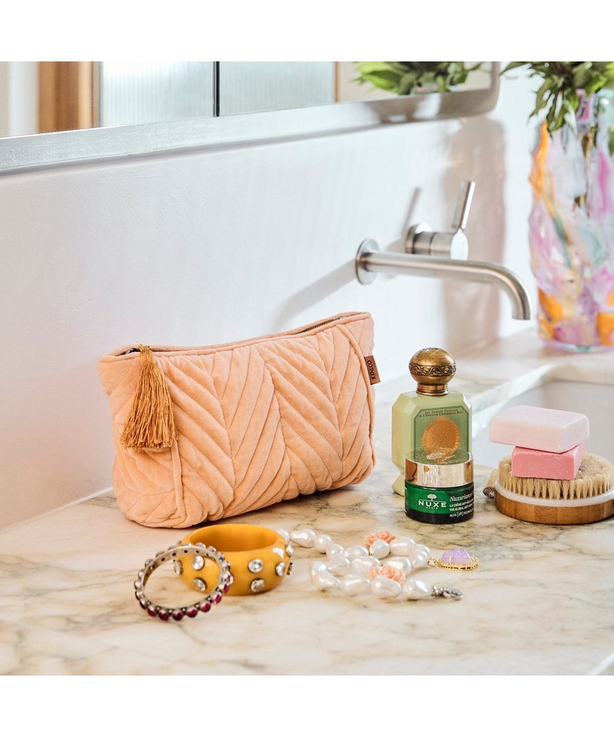 Kip&Co velvet toiletry bag in vibrant melon color with a soft fabric texture and zipper closure.