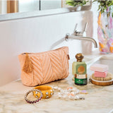 Kip&Co velvet toiletry bag in vibrant melon color with a soft fabric texture and zipper closure.
