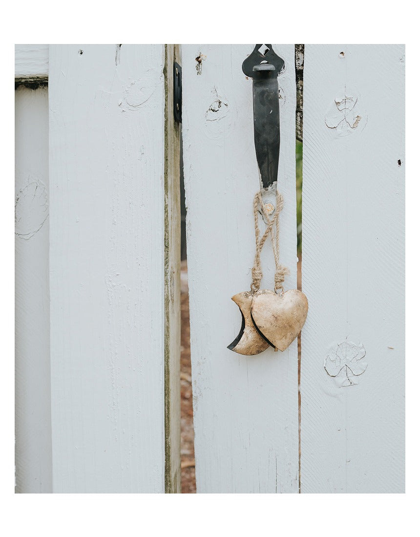 Matr Boomie Alaya Heart Wind Chime with metal and wood elements hanging from a string, designed to produce soothing sounds.
