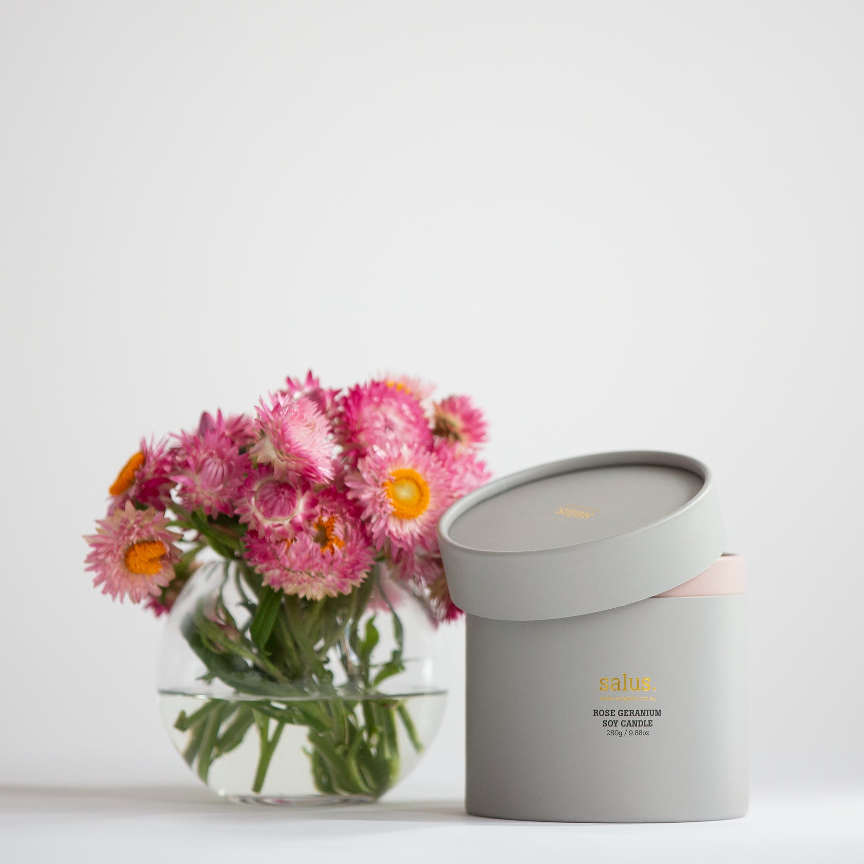 Salus Rose Geranium soy candle with a glass jar, featuring a floral label and a lit wick, designed for a 55-65 hour burn.