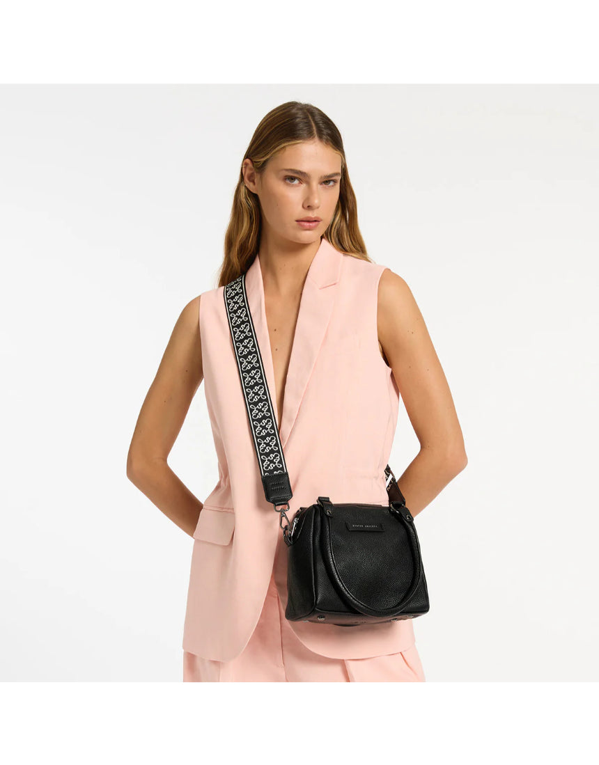 Black Status Anxiety Mini Mountains bag with adjustable strap and minimalist design, shown with casual outfit in lifestyle setting.