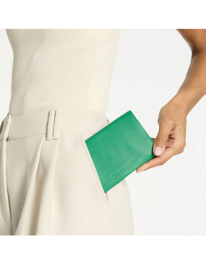 Status Anxiety Is Now Better Wallet in emerald green, showing a slim leather wallet with multiple card slots and a sleek design.