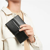 Black Status Anxiety Jonah Wallet with multiple card slots and cash compartments, shown in a lifestyle setting.