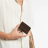 Status Anxiety Together For Now Cocoa wallet showing textured leather surface and stitched edges on a neutral background.