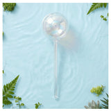 We The Wild self-watering globe plant accessory with clear glass bulb and stand, designed for automatic watering of indoor plants.