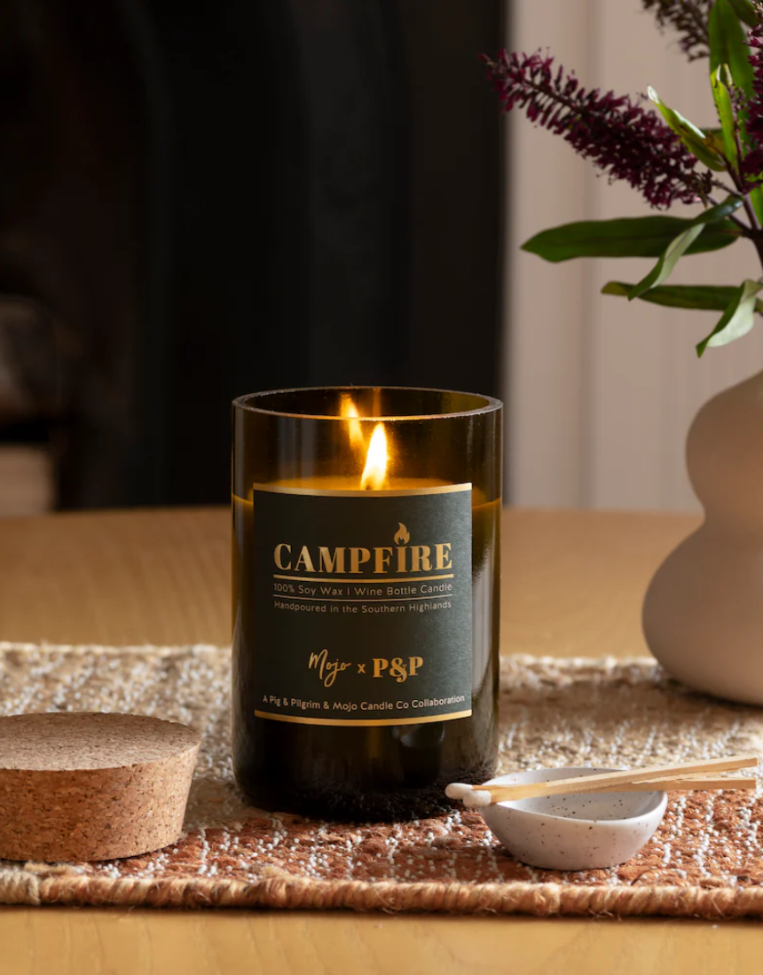 Mojo Candle Co. campfire scented candle in a glass jar, with a warm glow and wooden wick for cozy ambiance.