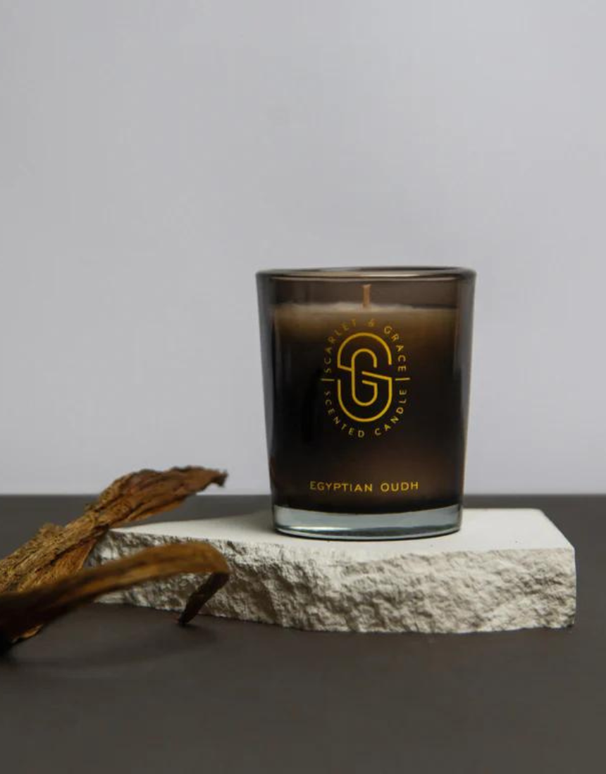 Scarlet & Grace Egyptian Oudh candle in a 60g glass jar with a lit wick, showcasing elegant design and warm amber glow.