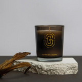 Scarlet & Grace Egyptian Oudh candle in a 60g glass jar with a lit wick, showcasing elegant design and warm amber glow.