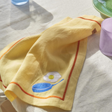 Kip & Co embroidered linen 4-piece breakfast napkin set with colorful "Breakfast Is Served" design on soft fabric.