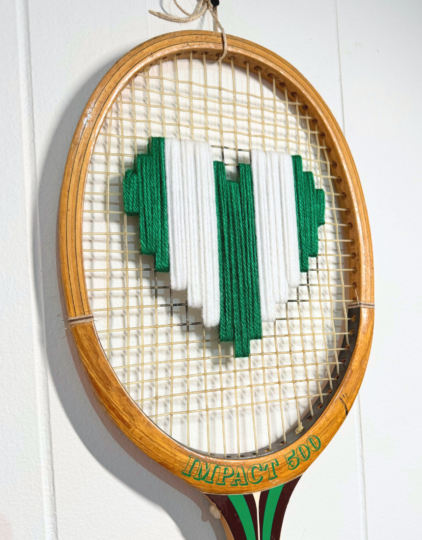 Green and white heart-shaped tennis racquet with "What A Racquet!" branding, featuring a playful and colorful design.