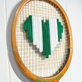 Green and white heart-shaped tennis racquet with "What A Racquet!" branding, featuring a playful and colorful design.