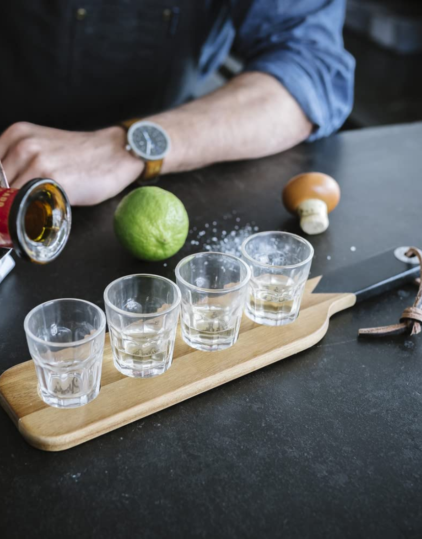 Gentlemen's Hardware shot glasses with a serving paddle, showcasing a rustic design and clear glass construction.