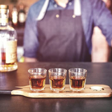 Gentlemen's Hardware shot glasses on a wooden serving paddle, ready for drinks, with a rustic, adventure-inspired design.