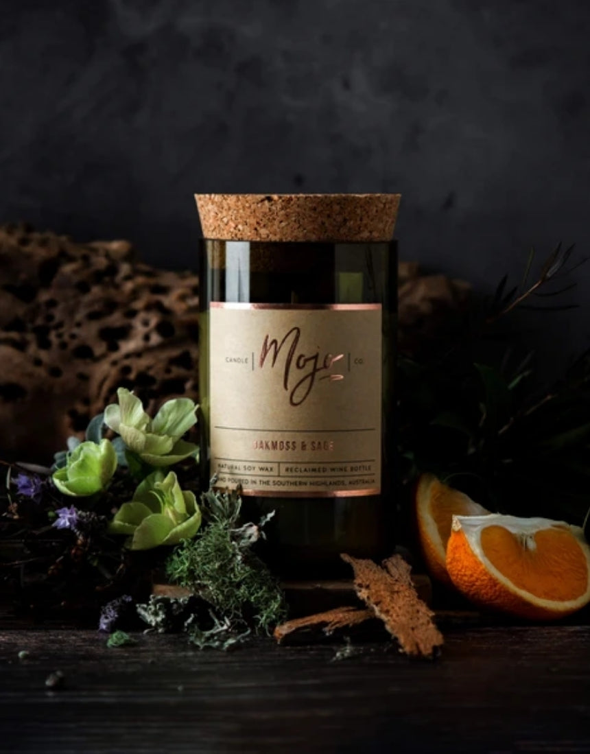 Mojo Candle Co. oakmoss and sage scented candle with a glass jar and wooden lid, showcasing natural botanical elements.